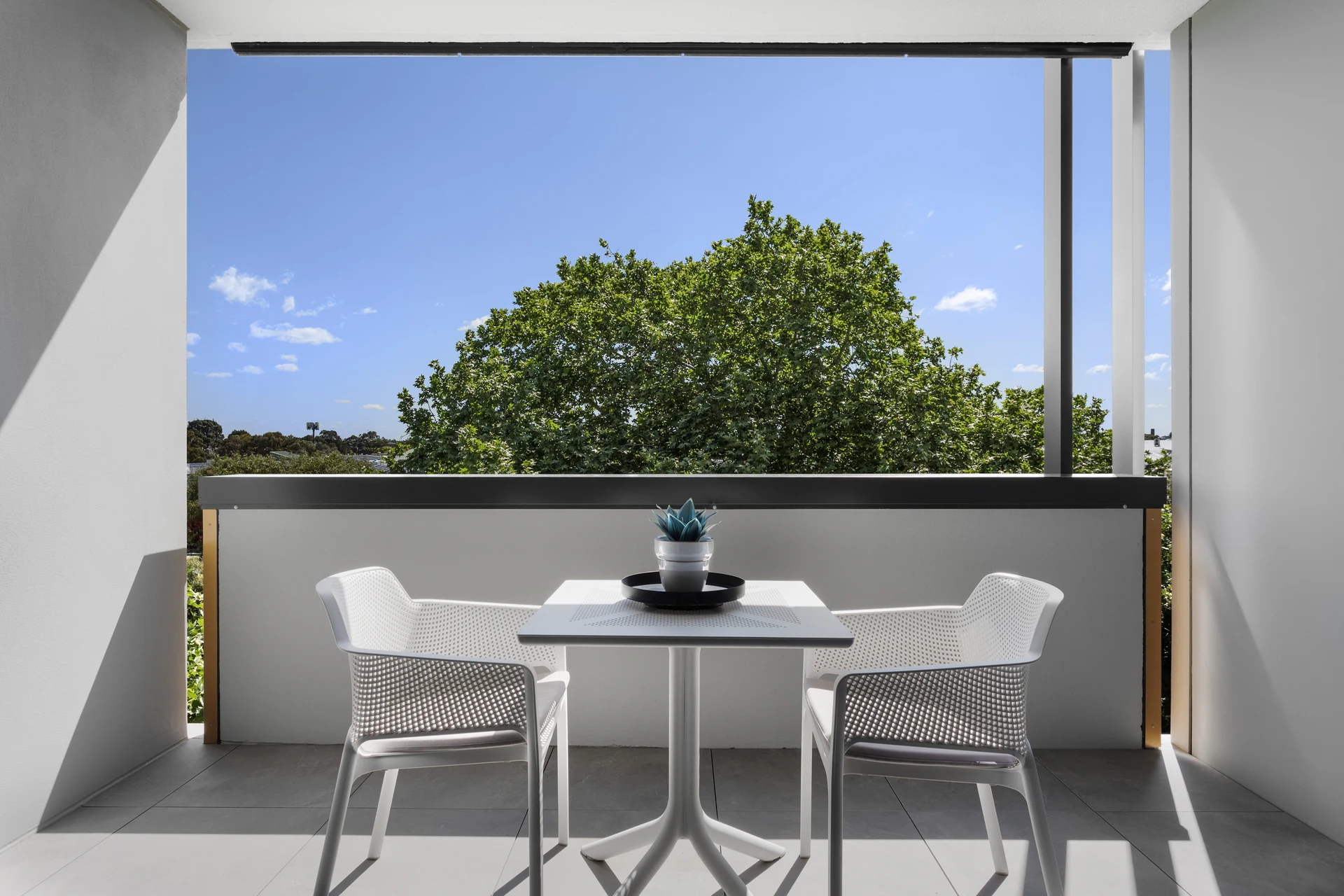 Sunlit private balcony at Teneo with outdoor seating and a leafy outlook