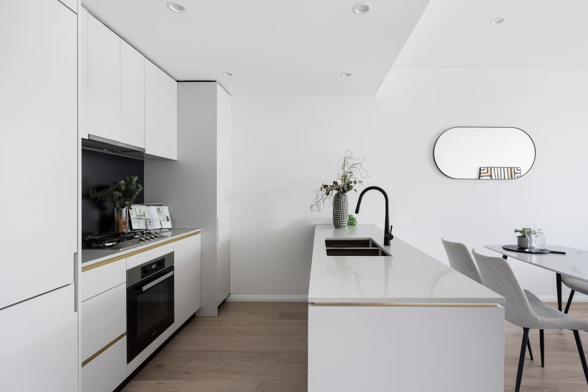 Teneo display apartment kitchen with white cabinetry, stone benchtop and dining area