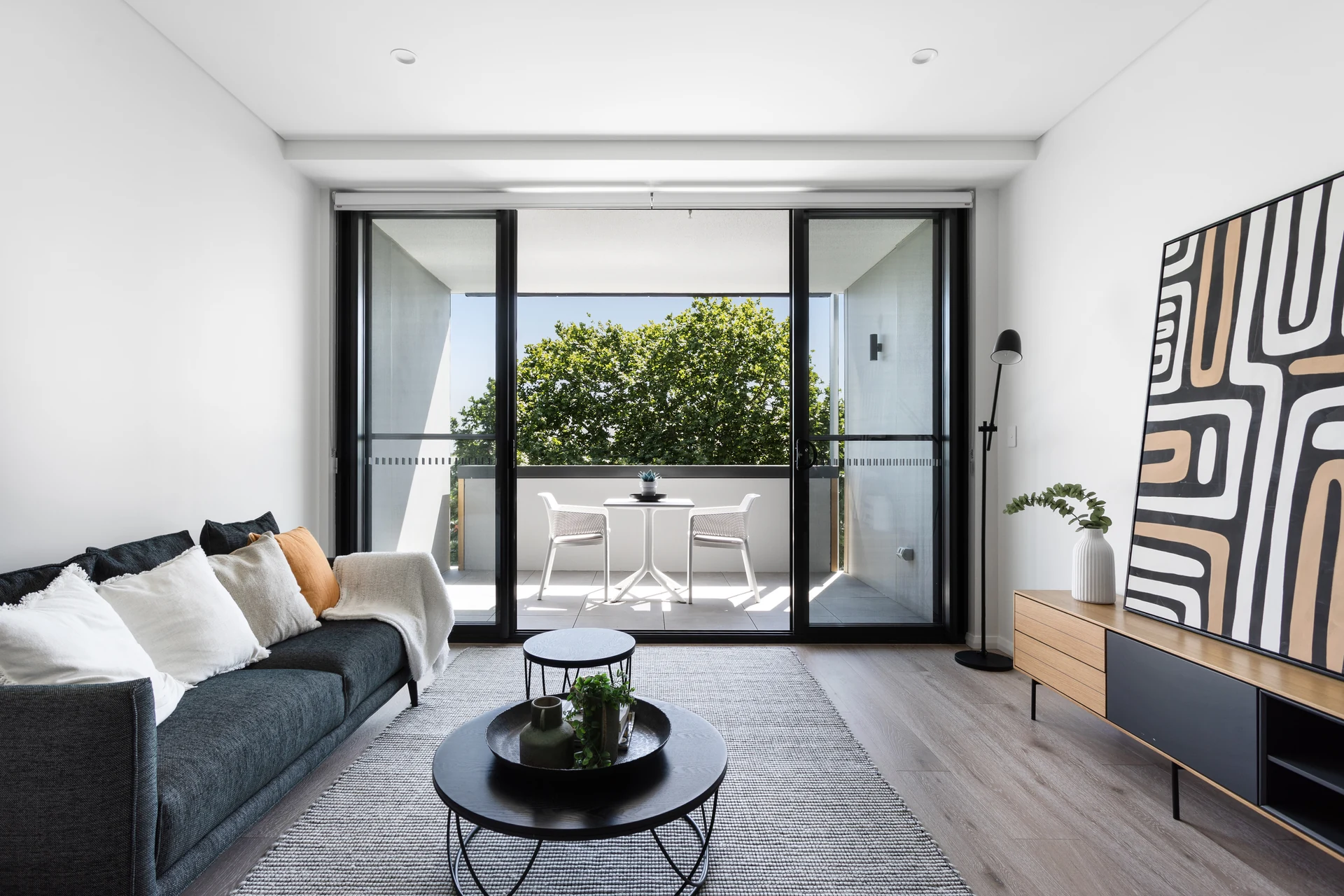 Sunlit Teneo living room opening onto a balcony with leafy views